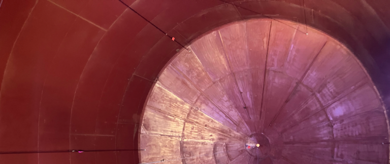 Interior view of a large, cylindrical metallic structure with a circular end and rods crossing overhead, reminiscent of the harmonious arrangement in a Colorado Choir performance.