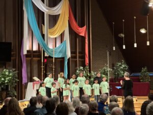 Kids singing in church with a colorful drape background.