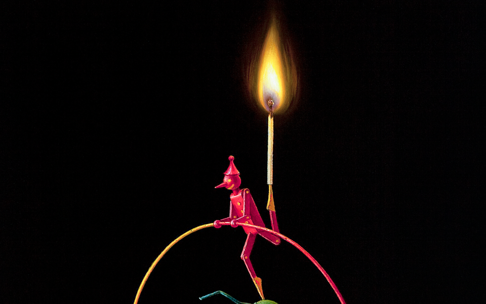 A small red figurine with a pointed hat balances on a curved wire, holding a lit matchstick upright—its flame evoking RubyFIRE—against a black background, capturing the essence of Shared Visions.