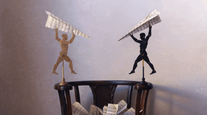 Two mannequin figures, one light and one dark, stand on a chair holding large paper airplanes made of sheet music, with more sheet music scattered below.