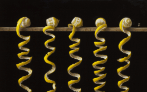 Five lemons are suspended on a wooden rod, each with a single continuous spiral peel hanging down against a black background.