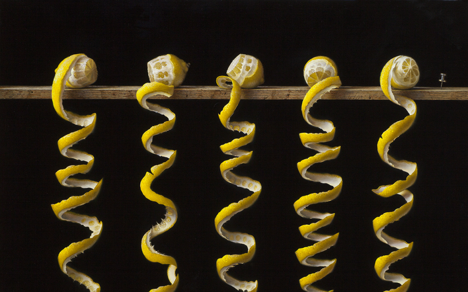 Five lemons with long, continuous peels spiral downward from a wooden rod against a black background.
