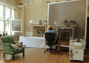 Get an inside peek into the world of Scott Fraser as an artist paints a detailed still life, while a dog lounges on a green chair in the well-lit studio.