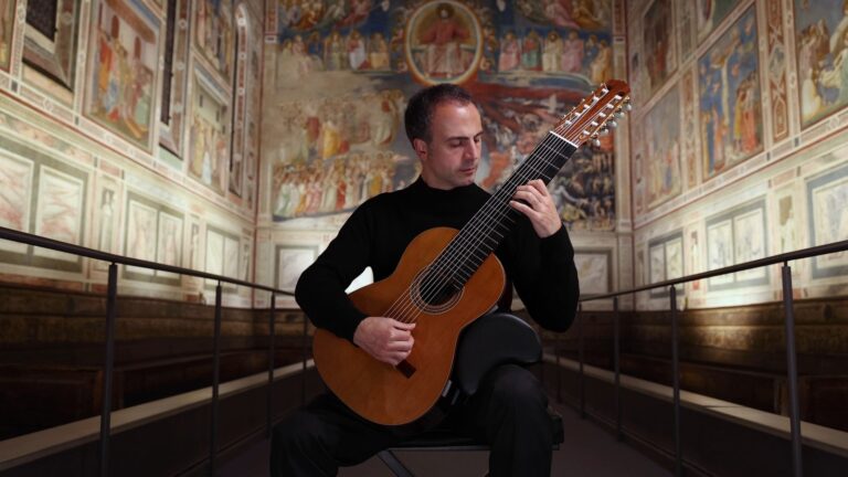 Nicolò Spera seated playing a ten-string classical guitar in the frescoed Scrovegni Chapel in Padua