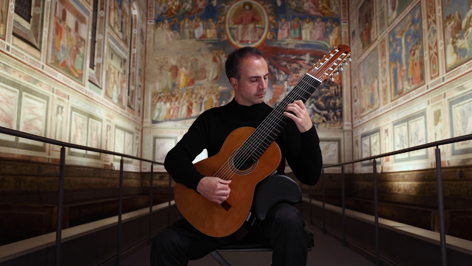 Nicolò Spera seated playing a ten-string classical guitar in the frescoed Scrovegni Chapel in Padua
