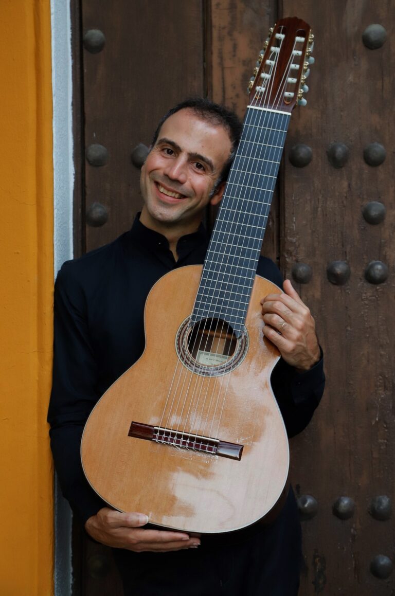 Portrait of guitarist Nicolò Spera smiling, holding his ten-string classical guitar in a doorway