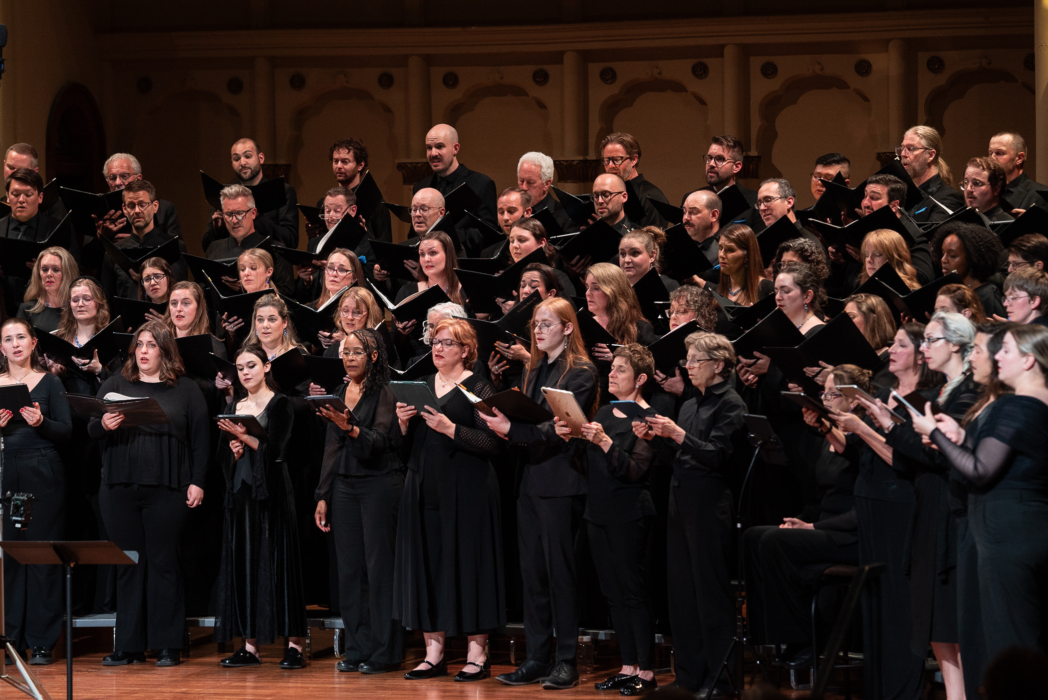 Ars Nova Singers performing in concert dress, holding black folders, filling the stage in rows