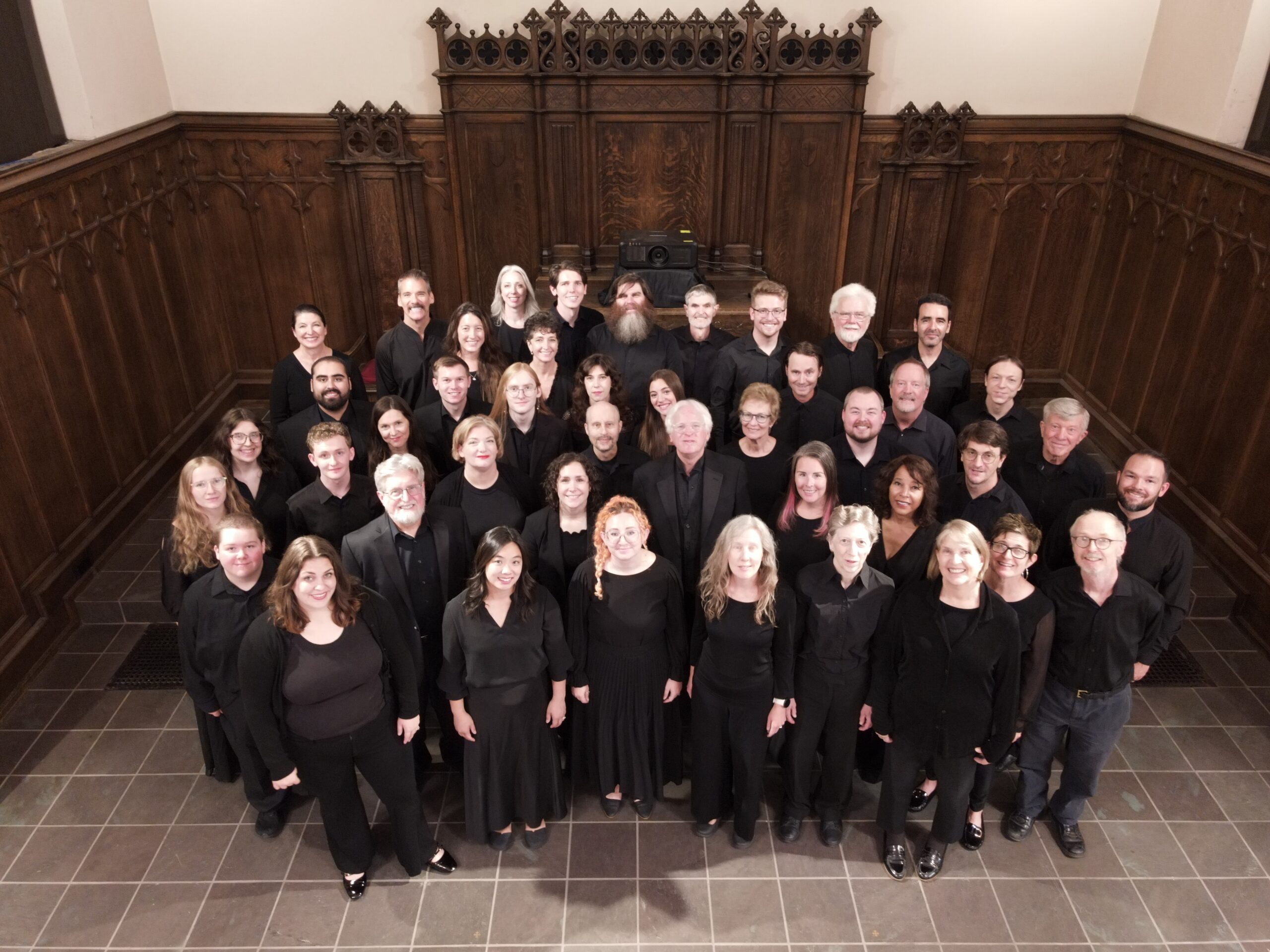 The Ars Nova Singers in concert black, gathered in a candlelit church sanctuary, seen from above